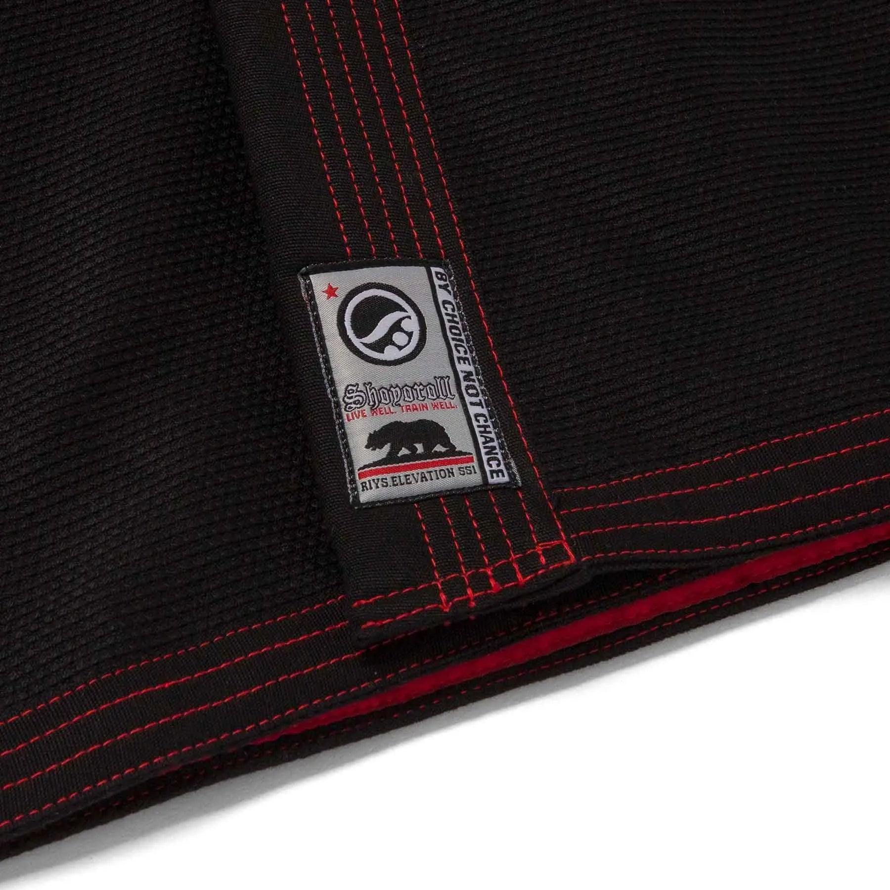 Close-up of a black martial arts gi with red stitching and a visible brand label.